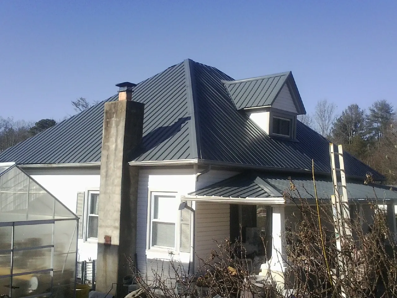 Dark blue standing seam metal roof on a white farmhouse with dormer — Slate & Tile Roof Repair by Roofing Brothers in Littleton