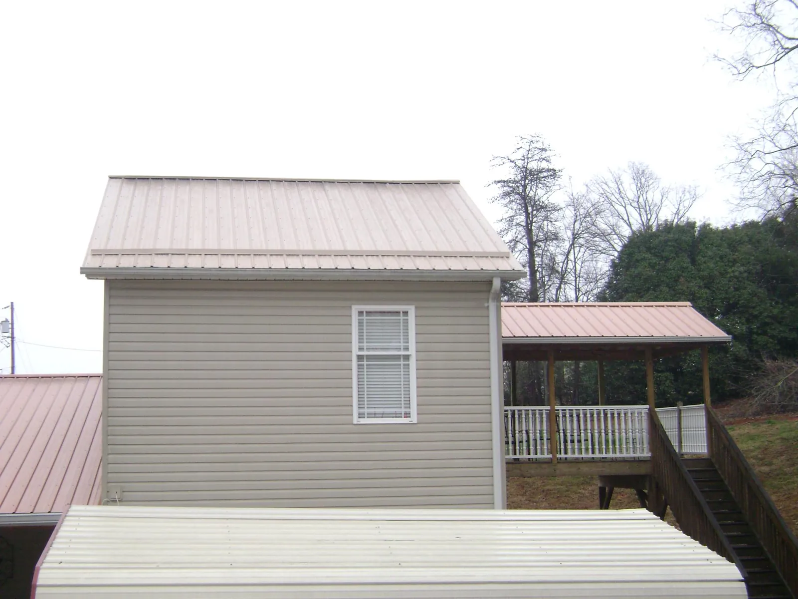 Tan metal roofs on a two story addition and attached porch, from a Roof Replacement job in Littleton
